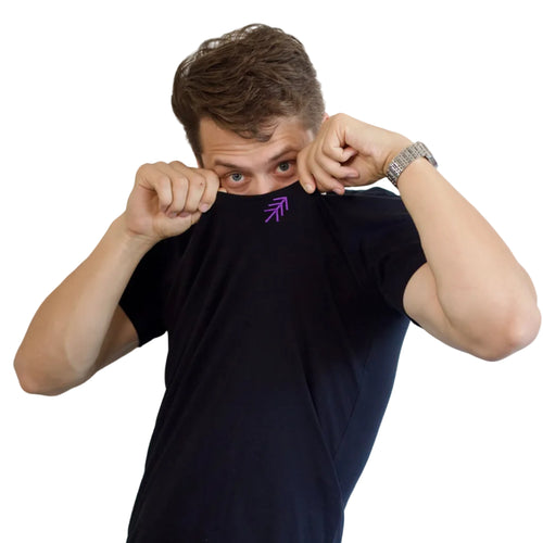 A dancer wearing a black t-shirt with a small purple pass logo embroidered on the chest, holding the collar up to show his eyes. He is wearing a silver watch on his wrist, set against a plain white background.