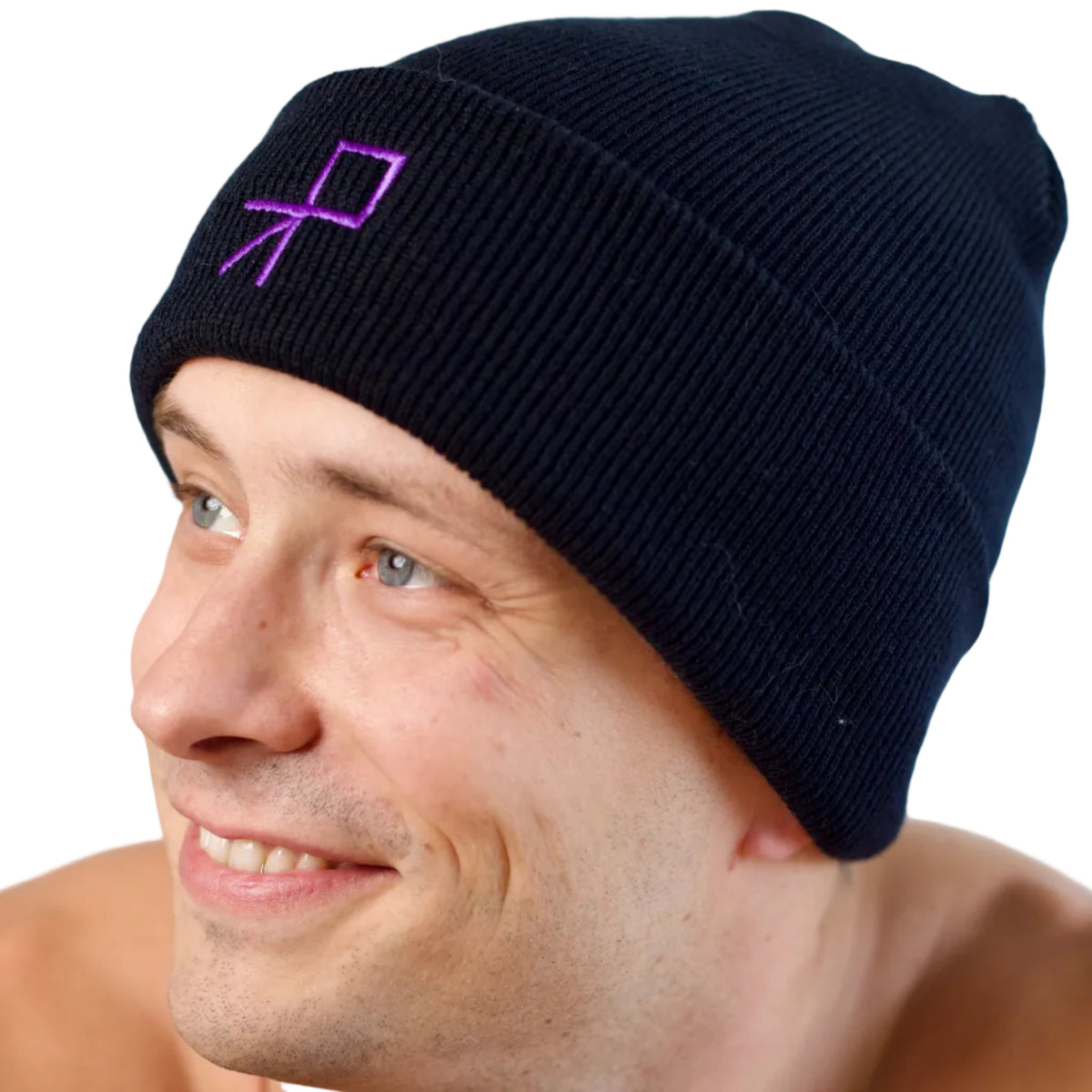 A three quarter view close-up of a smiling dancer wearing a black knit beanie with a purple embroidered geometric push logo on the front, set against a plain white background.