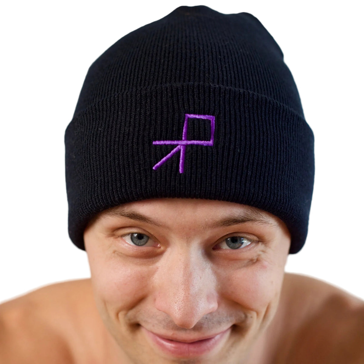 A close-up of a smiling dancer wearing a black knit beanie with a purple embroidered geometric push logo on the front, tipping his head towards the camera, set against a plain white background.