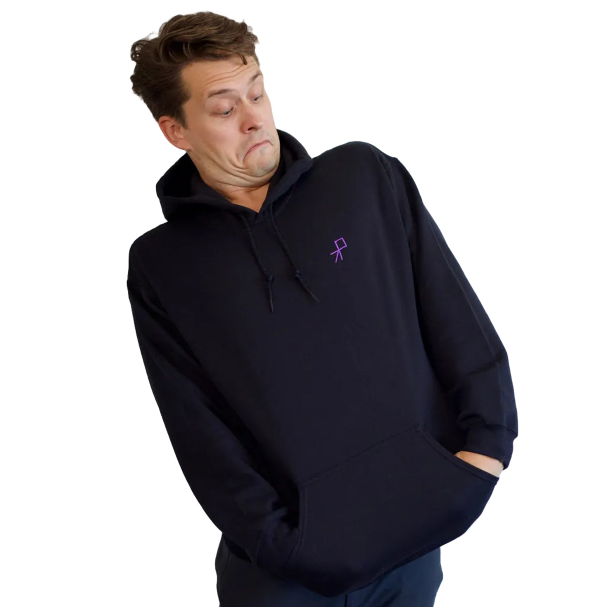 A dancer wearing a black pullover hoodie with a small purple embroidered pass graphic on the left chest, posed against a plain off-white wall. He is looking down at the logo with an impressed look.