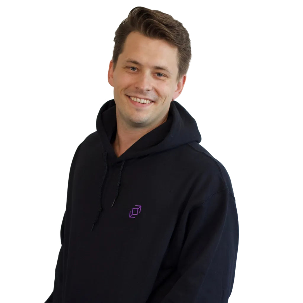 A smiling dancer with short brown hair wearing a black push pass whip pullover hoodie with a small purple geometric whip logo on the left chest, standing against a plain white background.