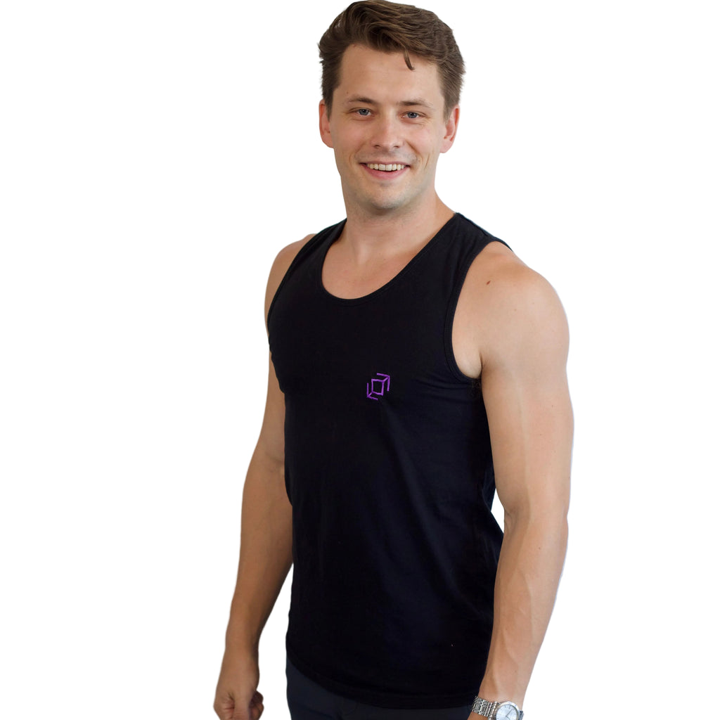 A smiling dancer wearing a black Push Pass Whip sleeveless tank top with a small purple geometric whip logo on the left chest, standing against a plain white wall.